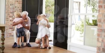 Visiting grandparents bend and kneel to hug grandchildren