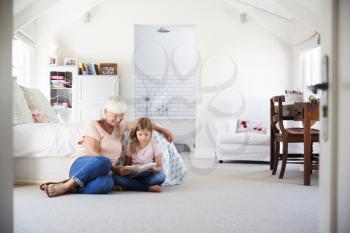 Grandmother and granddaughter reading a book in her bedroom