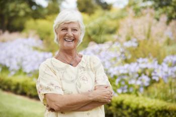Portrait Of Senior Woman Enjoying Walk By Flower Beds In Park