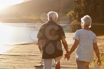 Romantic Senior Couple Walking On Wooden Jetty By Lake