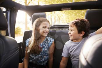 Children Sitting In Back Seat Of Open Top Car On Road Trip