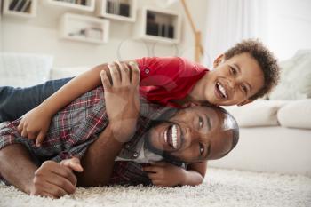Son Climbs On Fathers Back As They Play Game In Lounge Together