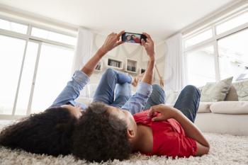 Mother And Son Lying On Rug And Posing For Selfie At Home