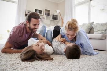 Parents Tickling Children As They Play Game In Lounge Together