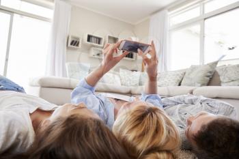Mother And Children Lying On Rug And Posing For Selfie At Home