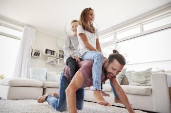 Father Giving Children Ride On Back In Lounge At Home