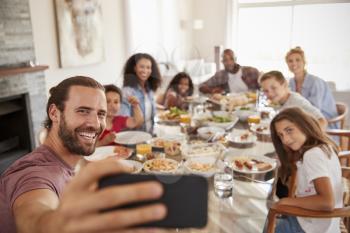 Two Families Taking Selfie As They Enjoy Meal At Home Together