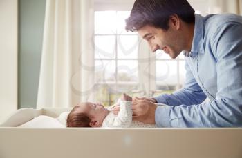 Father Playing With Newborn Baby Lying On Changing Table