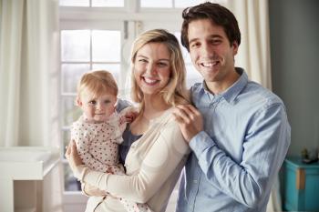 Portrait Of Smiling Family Holding Baby Daughter In Nursery