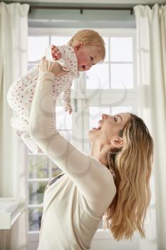 Mother Lifting Baby Daughter In The Air In Nursery