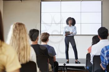 Female Teacher With Digital Tablet Giving Presentation To High School Class In Front Of Screen