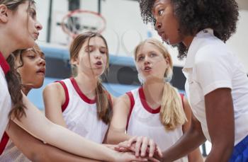 Female High School Basketball Players Joining Hands During Team Talk With Coach