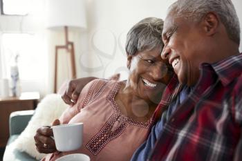 Loving Senior Couple Sitting On Sofa At Home Relaxing With Hot Drink