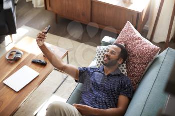 Overhead View Of Man Lying On Sofa At Home Posing For Selfie On Mobile Phone