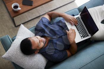 Overhead View Of Man Lying On Sofa At Home Using Laptop Computer