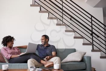 Couple Sitting On Sofa At Home With Woman Using Laptop Computer