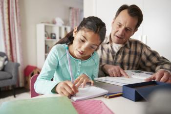 Grandfather Helping Granddaughter With Homework Sitting At Desk In Bedroom