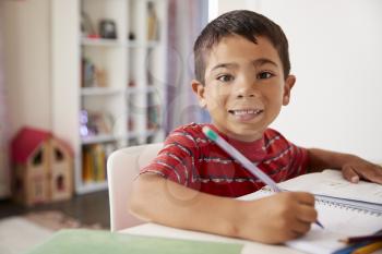 Portrait Of Young Boy Sitting At Desk In Bedroom Doing Homework