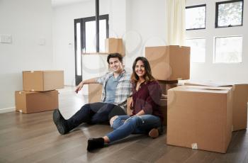 Portrait Of Happy Couple Sitting On Floor Surrounded By Boxes In New Home On Moving Day