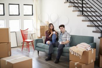 Portrait Of Happy Couple Resting On Sofa Surrounded By Boxes In New Home On Moving Day