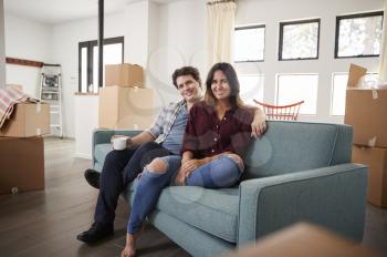Portrait Of Happy Couple Resting On Sofa Surrounded By Boxes In New Home On Moving Day