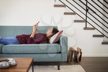 Side View Of Woman Lying On Sofa At Home Using Mobile Phone