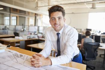 Young male architect leaning on desk smiling to camera