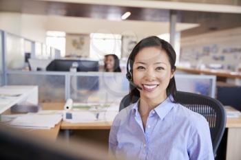 Young Asian woman working in a call centre smiling to camera