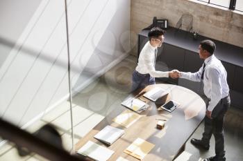 Two businessmen stand shaking hands in office, elevated view