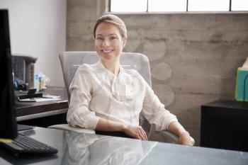 Young white woman sitting at office desk smiling to camera