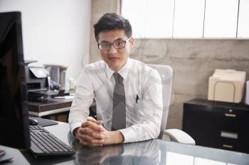 Young Asian businessman at an office desk, looking to camera