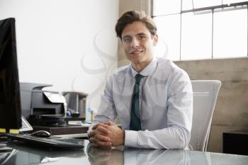 Young white businessman at an office desk, smiling to camera
