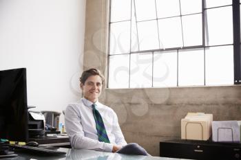 Young white businessman sitting in office smiling to camera