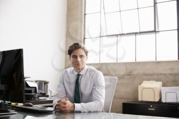 Young businessman sitting at office desk smiling to camera