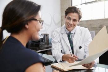 White male doctor showing file to female patient in office