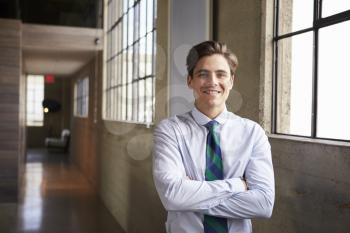 Young white businessman stands smiling with arms crossed