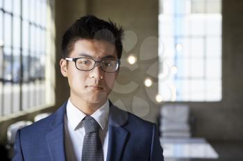 Young Asian businessman looking to camera, head and shoulders