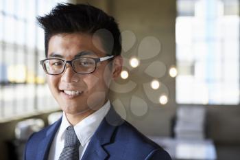 Young Asian businessman smiling to camera, head and shoulders