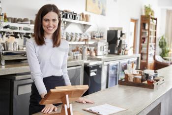 Young female coffee shop owner behind the counter, smiling
