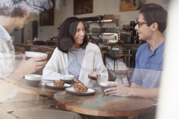 Three happy young adult friends sit talking at a coffee shop
