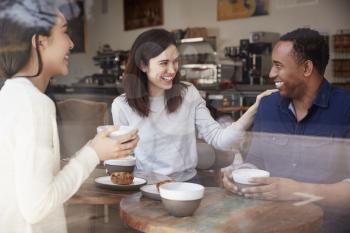 Three friends having coffee and laughing at a coffee shop