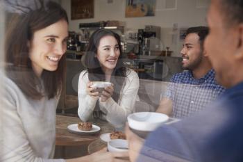 Four smiling adult friends sit having coffee at coffee shop