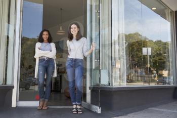 Two young female coffee shop owners stand outside their shop