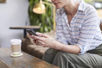 Young woman using smartphone in a coffee shop, mid section