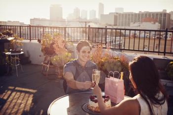 Couple Making Toast To Celebrate Birthday On Rooftop Terrace With City Skyline In Background