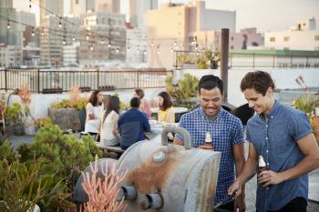 Friends Gathered On Rooftop Terrace For Barbecue With City Skyline In Background