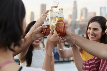 Female Friends With Drinks Making A Toast On Rooftop Terrace For Party With City Skyline In Background