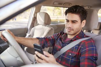Young man in car checking his smartphone while driving