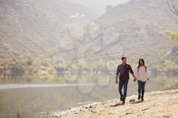Young couple walk holding hands by a mountain lake