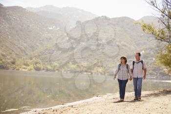 Senior couple hold hands hiking by mountain lake, front view